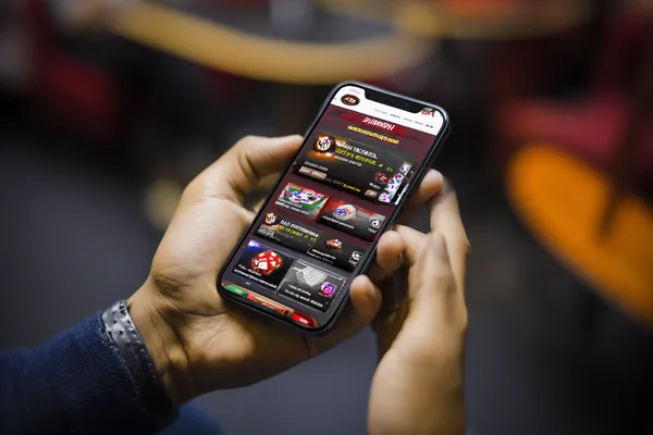 Um homem concentrado em seu laptop com estatísticas ao vivo ao fundo, destacando os recursos dedicados de esportes e jogos do app móvel 615BET.